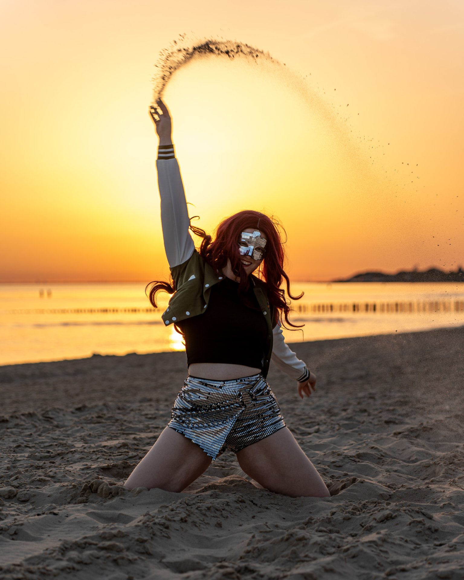Danseres met spiegelmasker gooit zand omhoog bij zonsondergang